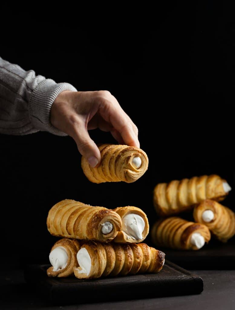 A woman's hand holds a baked tube with whipped protein cream, black background